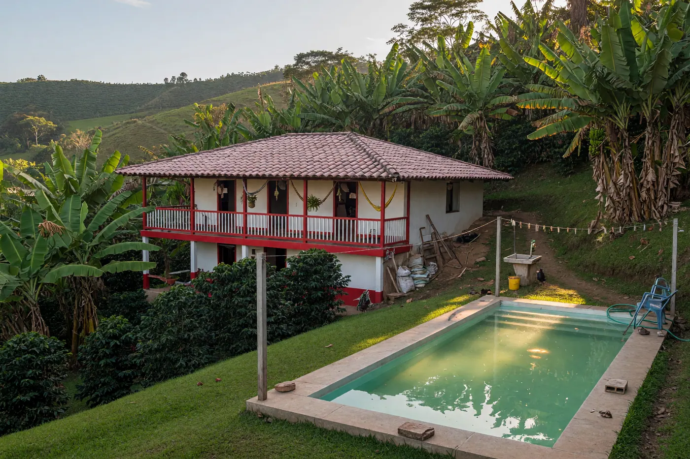Finca cafetera colombiana con balcón rojo, piscina y vegetación de plátano