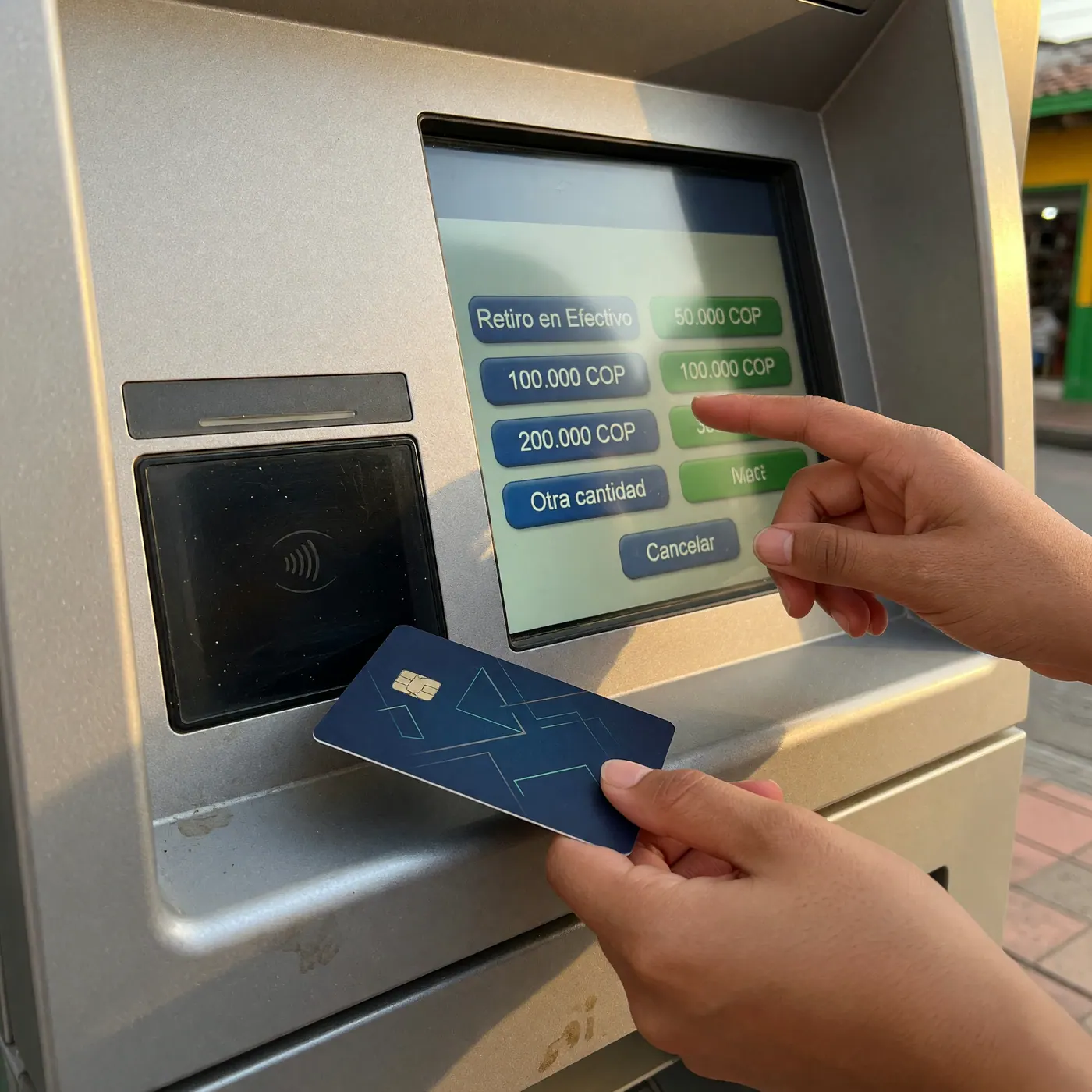 Hands using an ATM screen with Colombian peso withdrawal options and a contactless debit card