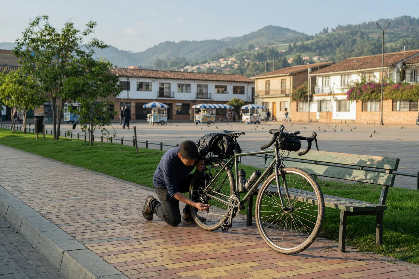 A person inspecting a mid-range bicycle beside a bench on a sunny Bogotá plaza