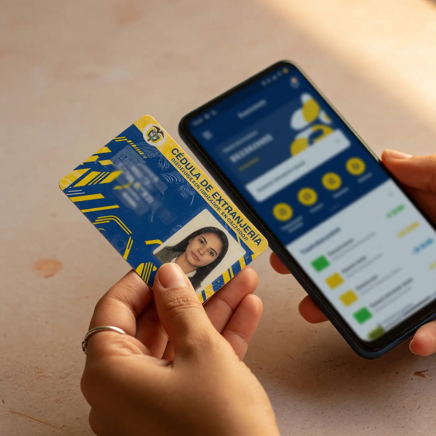 A hand holding a Colombian Cédula de Extranjería ID card next to a smartphone showing a mobile banking app interface