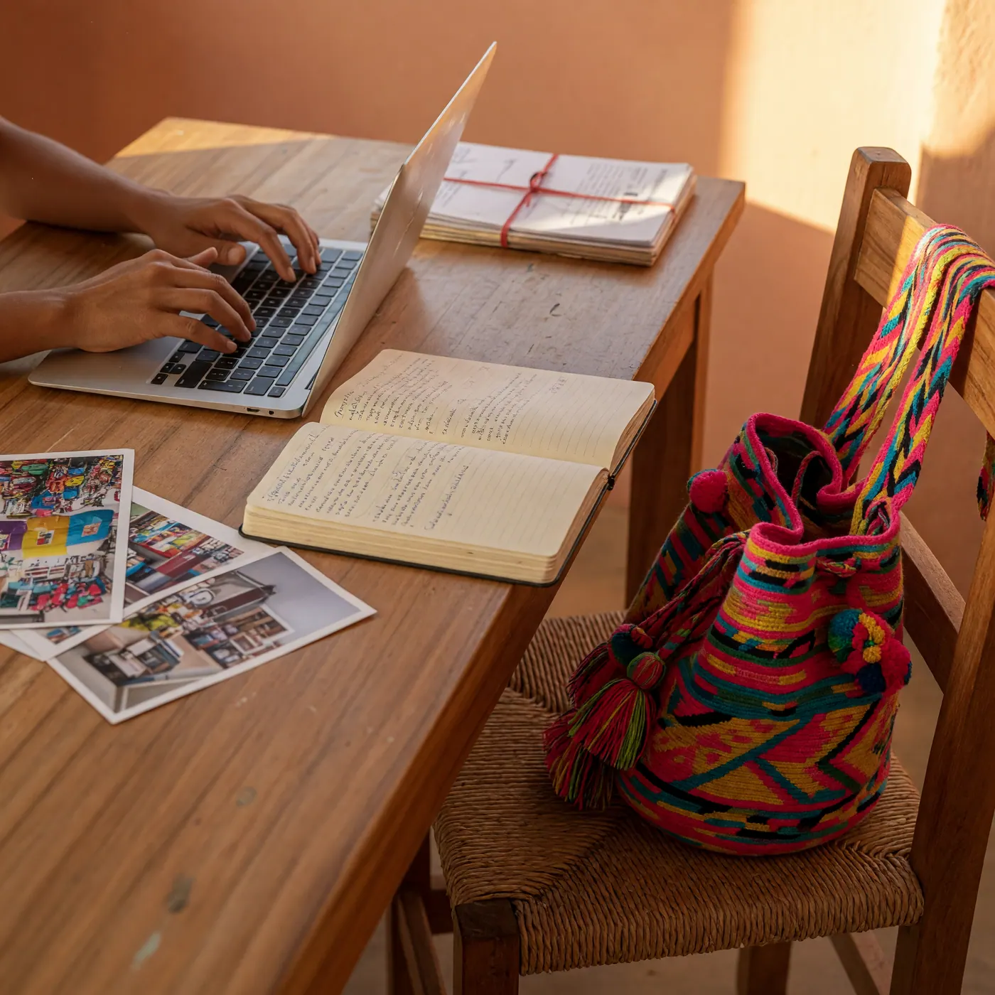 Manos sobre un teclado junto a cuaderno de notas en español y bolso artesanal colombiano Wayuu, ambiente de trabajo local cartagenero