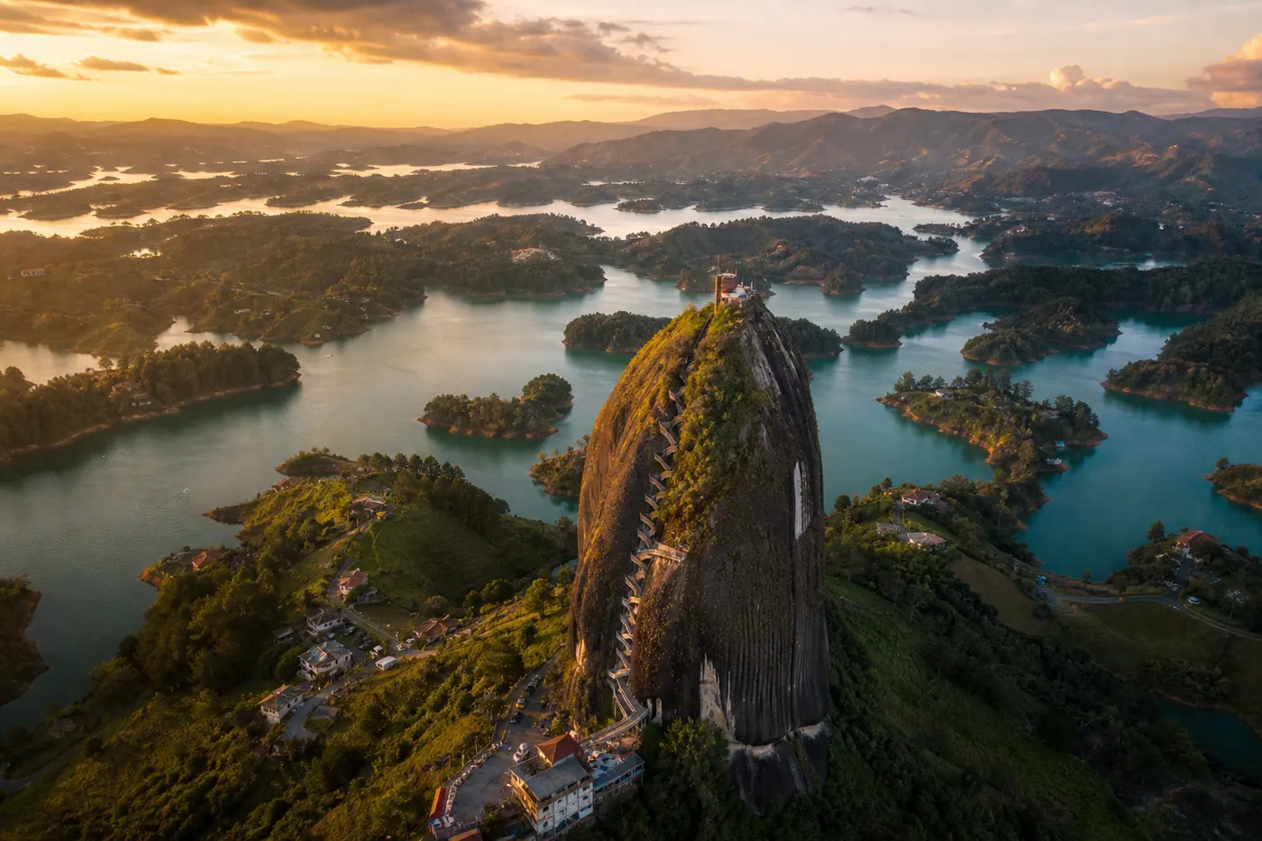 Aerial view of El Peñol monolith rising above the Guatapé reservoir in Colombia, surrounded by green islands at golden hour