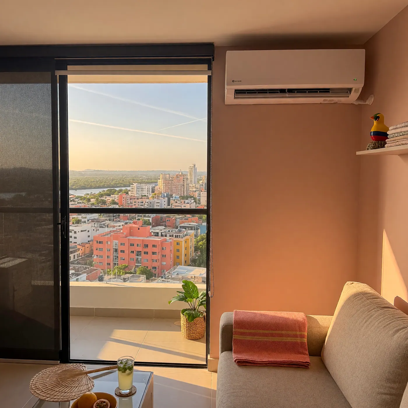 Wall-mounted split air conditioner inside a sunlit apartment living room overlooking a Colombian city