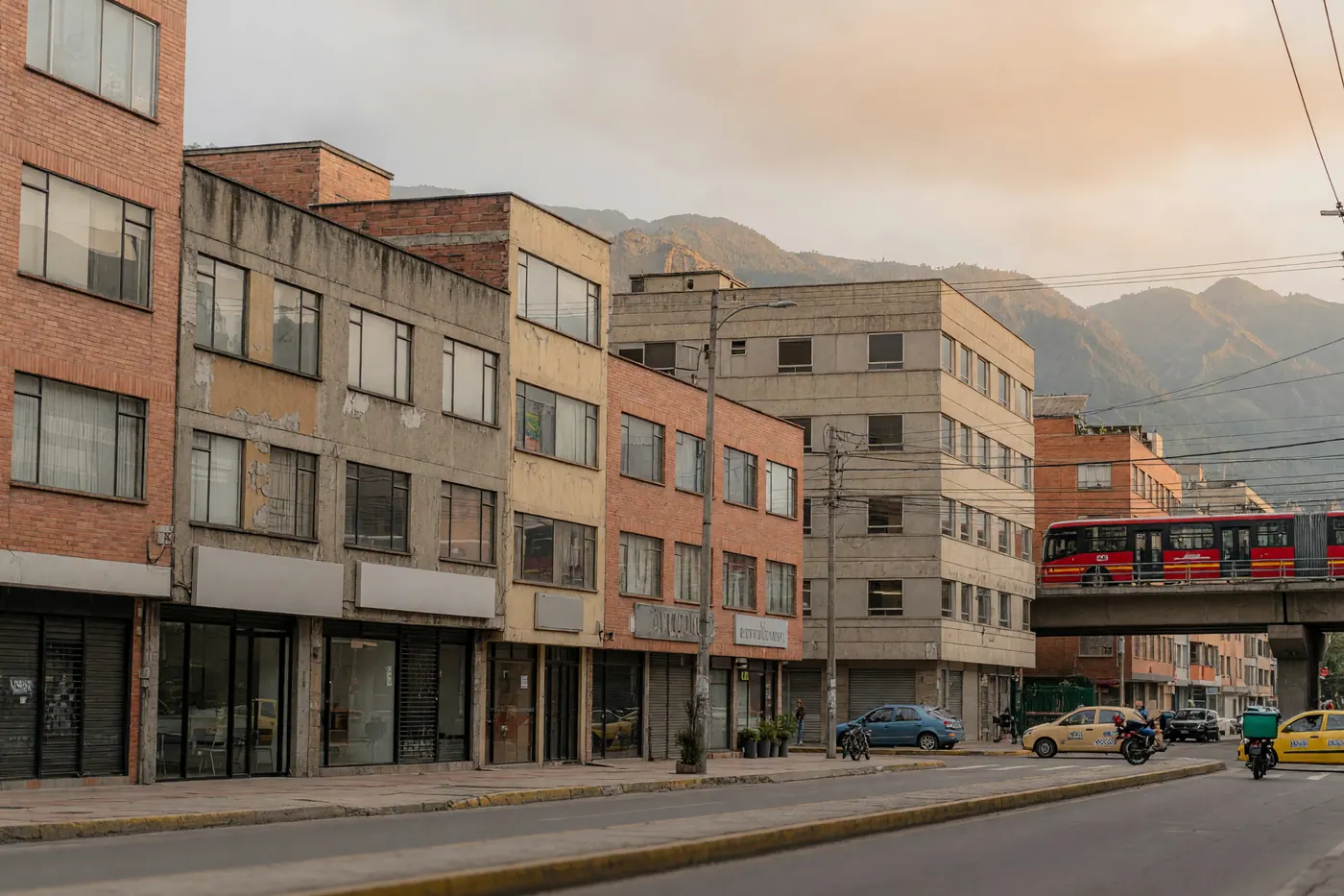 Mid-rise brick and concrete office street under highland haze with mixed traffic on a wide avenue, no readable brand names
