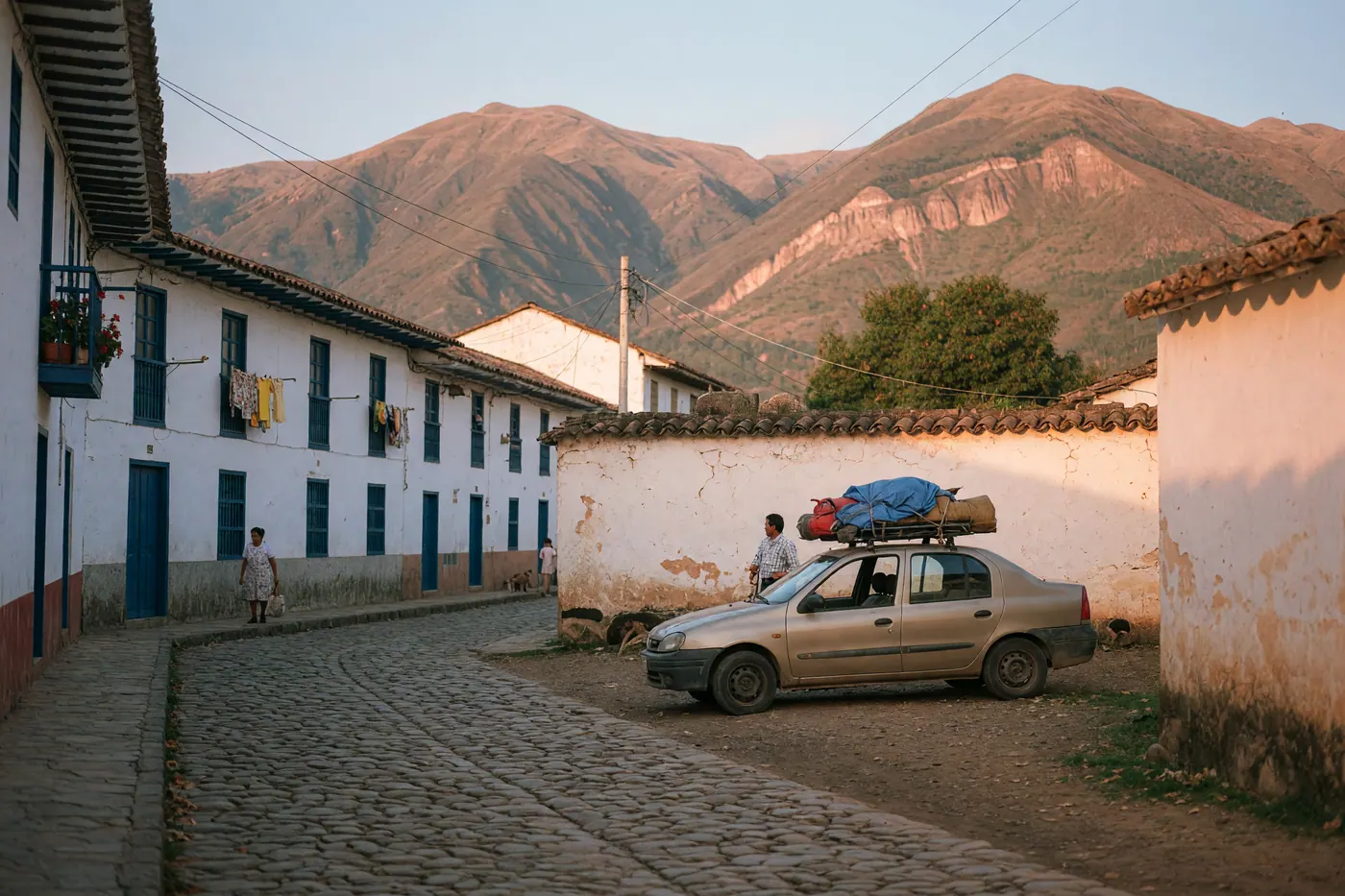 Calle empedrada con casas coloniales blancas, montañas y un carro de viaje