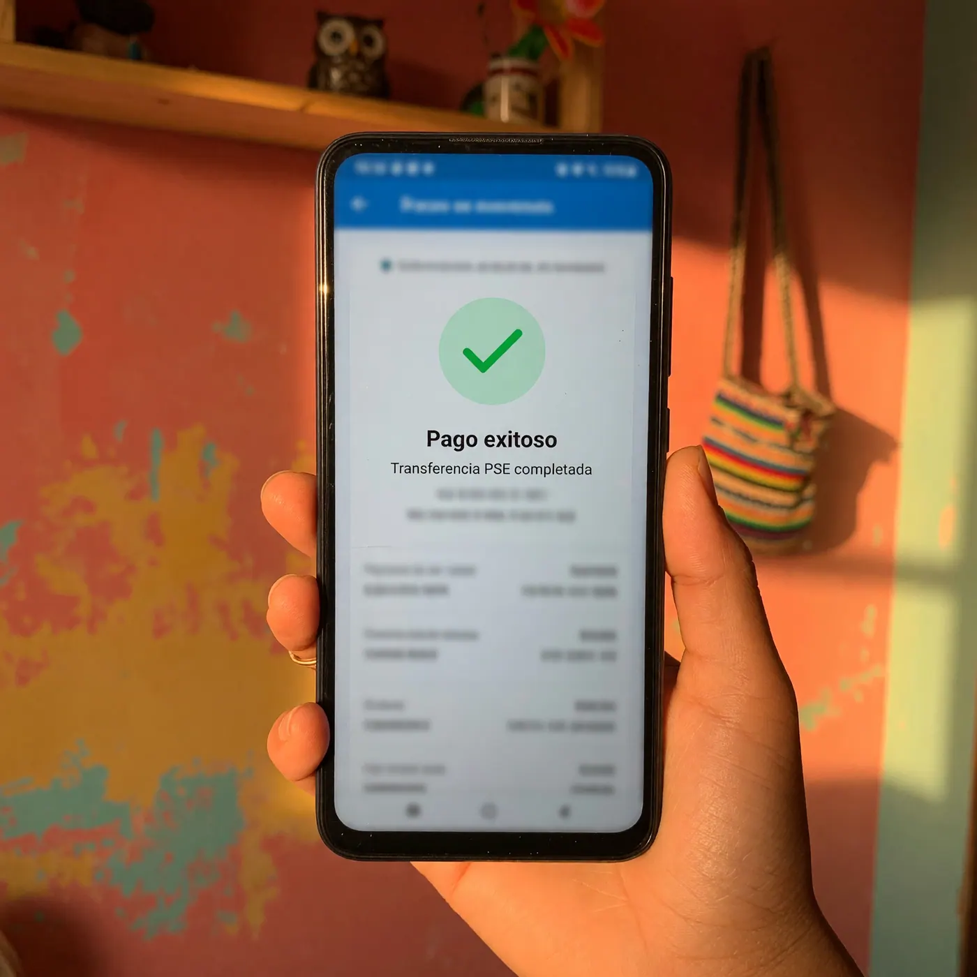 Smartphone con pantalla de confirmación de pago PSE exitoso sostenido en una vivienda colombiana