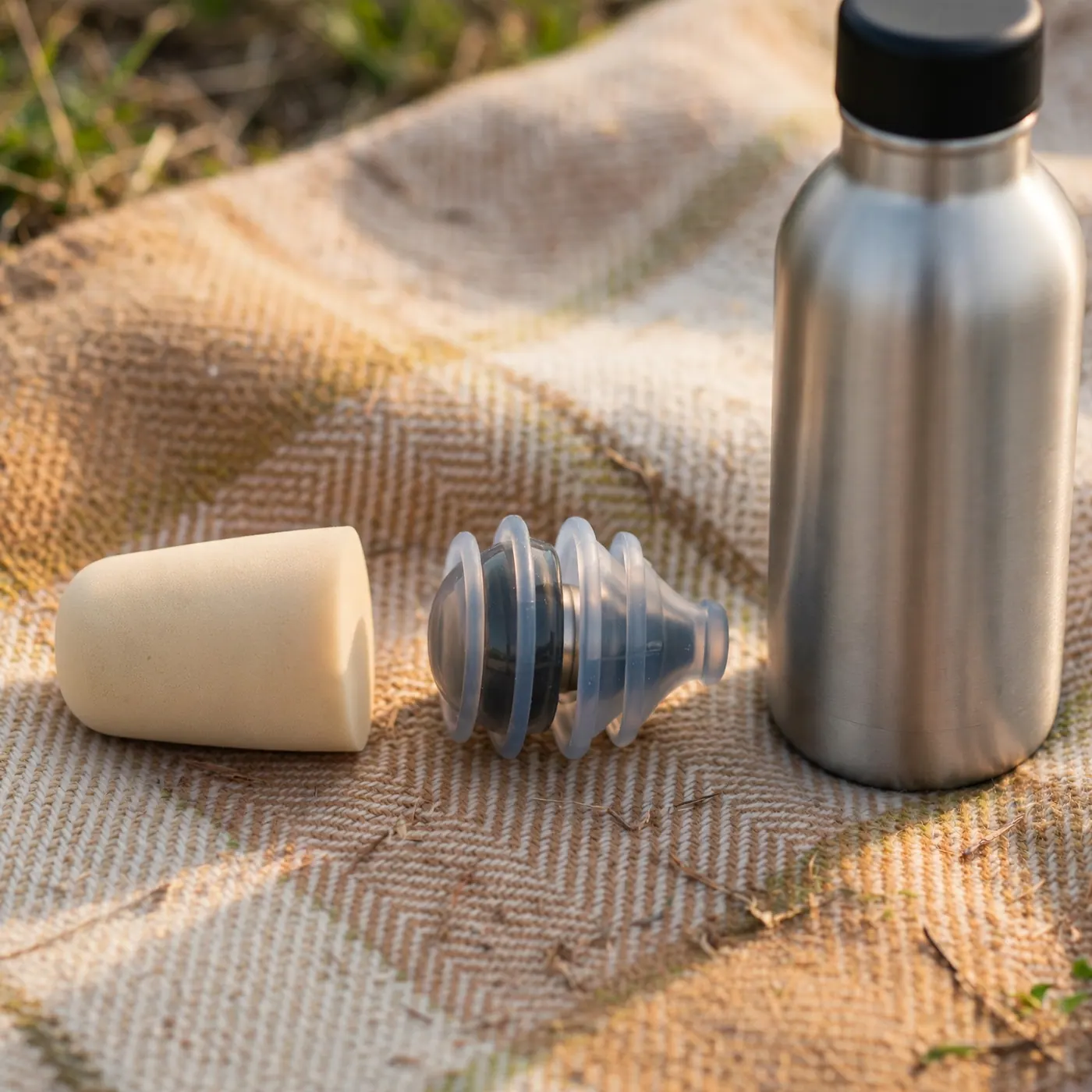 Tapón de espuma y tapón con filtro sobre una manta de picnic junto a una botella de agua reutilizable