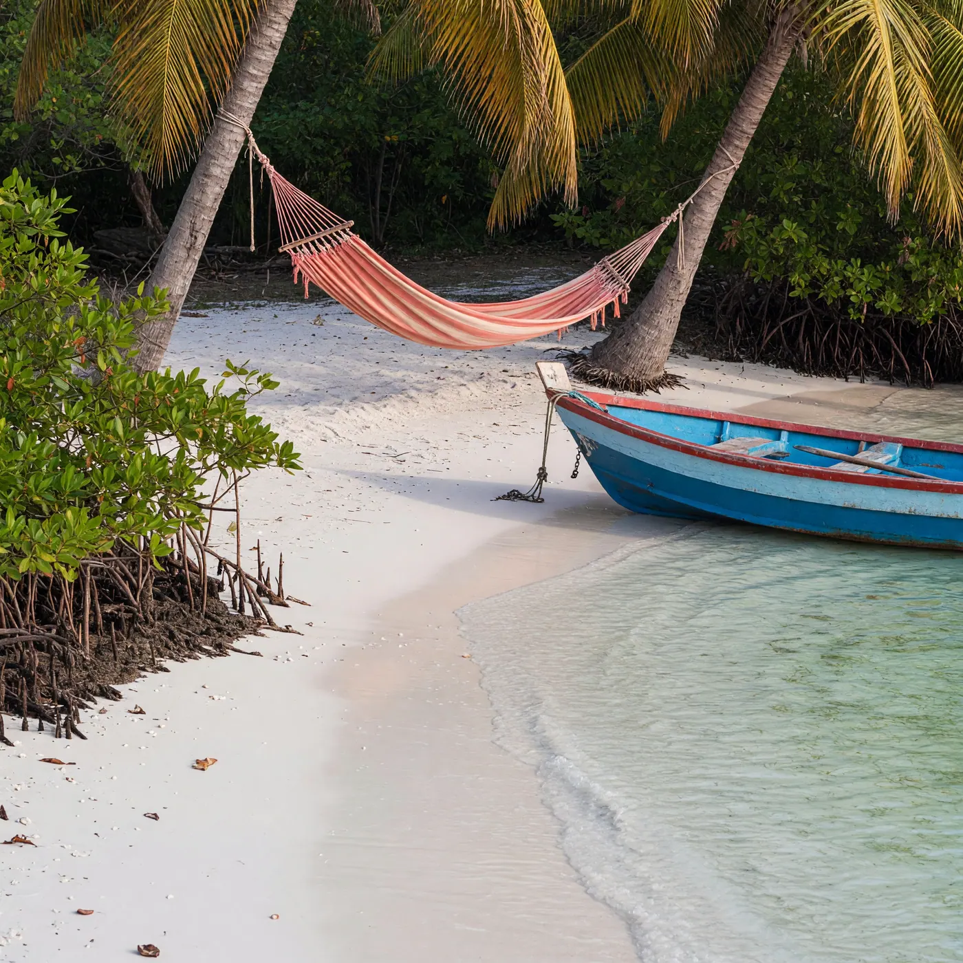 Playa de arena blanca en una isla del archipiélago de San Bernardo con una lancha de madera, manglar y una hamaca entre palmeras