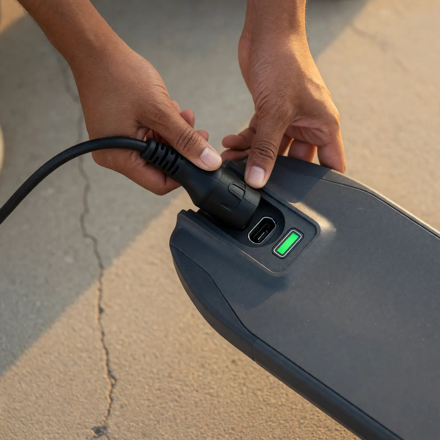 Manos conectando un cargador al puerto de carga de un scooter eléctrico