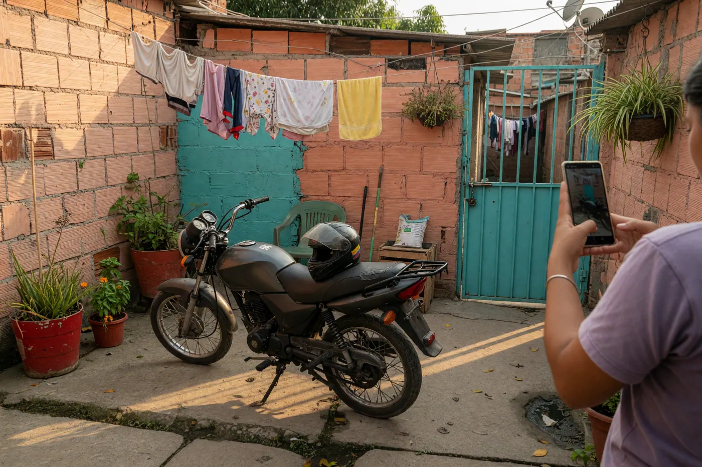 Moto pequeña de trabajo en un patio residencial con casco en el asiento y alguien fotografiándola con el celular