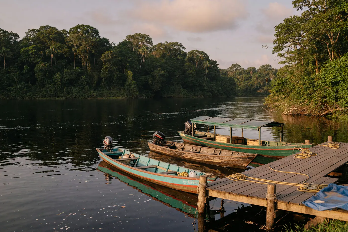 Muelle fluvial de madera en Inírida con lanchas amarradas sobre el río de aguas oscuras y selva tropical al fondo bajo un cielo nublado