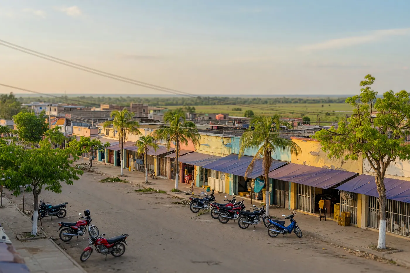 Calle cotidiana de Yopal, Casanare, con amplio cielo llanero, motos y negocios bajo árboles de sombra