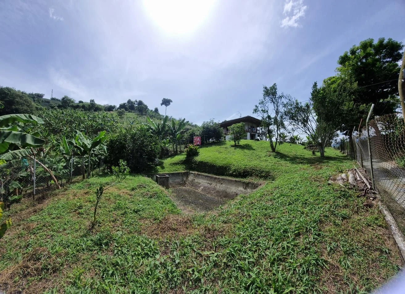 Estanque piscícola de la finca con la casa campesina en la colina al fondo